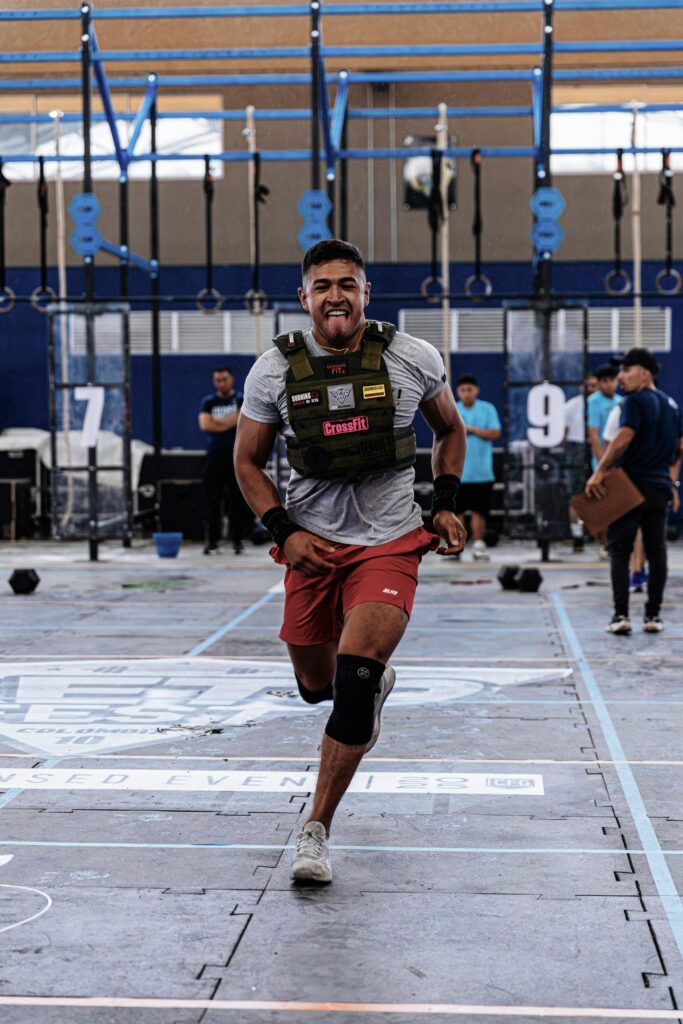 Young athlete competing in CrossFit event, wearing weighted vest and knee brace outdoors.
