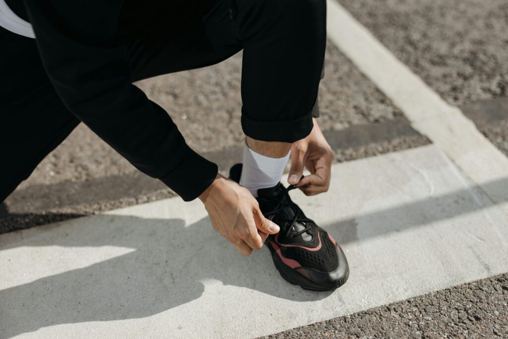 Close-up of a person tying their sneaker on an outdoor pavement with road markings.